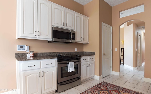 kitchen with white cabinetry, light tile flooring, stainless steel appliances, dark stone countertops, and a textured ceiling