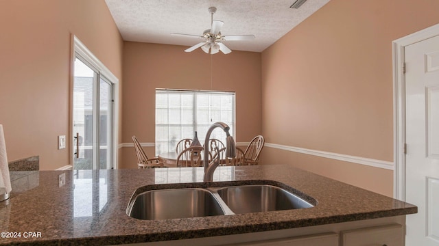 kitchen featuring dark stone counters, a textured ceiling, ceiling fan, and sink