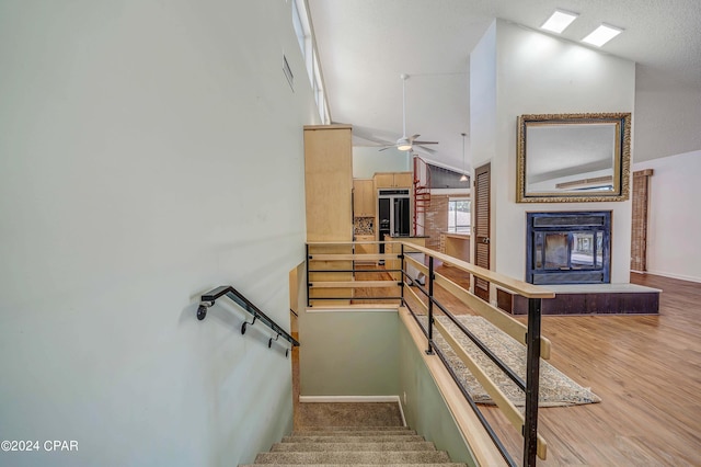 staircase with wood-type flooring, high vaulted ceiling, and ceiling fan