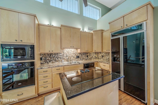 kitchen with dark stone counters, black appliances, a towering ceiling, and light brown cabinets