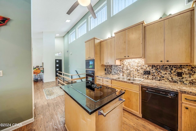 kitchen with black appliances, a towering ceiling, light brown cabinets, and light hardwood / wood-style flooring