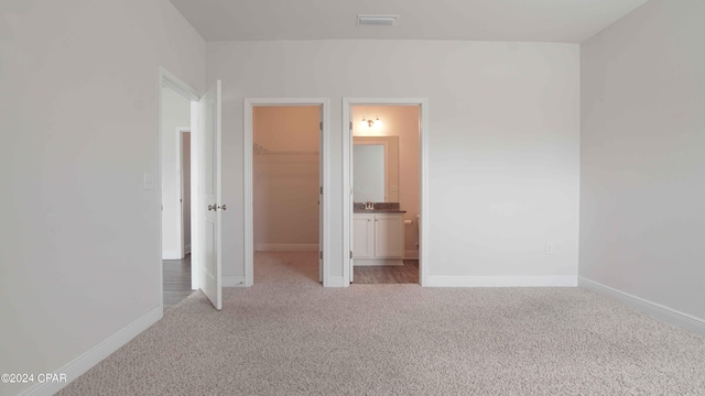 unfurnished bedroom featuring a walk in closet, ensuite bathroom, a closet, and light carpet