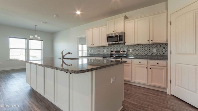 kitchen featuring decorative light fixtures, sink, backsplash, stainless steel appliances, and a center island with sink