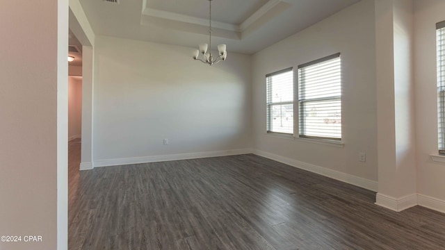 empty room with dark hardwood / wood-style floors, a tray ceiling, a chandelier, and crown molding