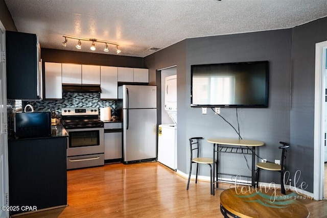 kitchen featuring tasteful backsplash, stacked washer / dryer, a textured ceiling, appliances with stainless steel finishes, and light wood-type flooring