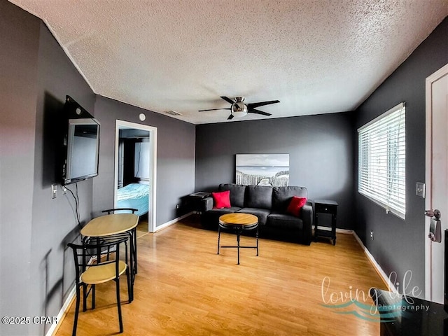 living room featuring ceiling fan, a textured ceiling, and light wood-type flooring