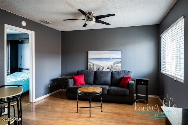 living room featuring ceiling fan, a textured ceiling, and light wood-type flooring