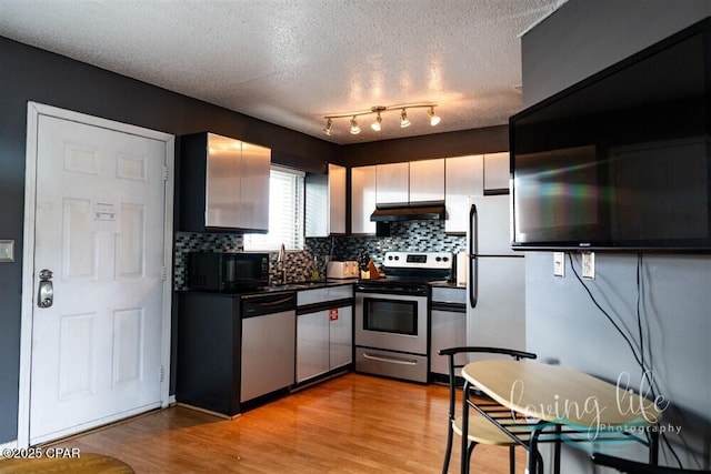 kitchen featuring sink, light wood-type flooring, a textured ceiling, appliances with stainless steel finishes, and tasteful backsplash