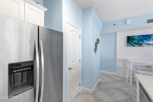 kitchen with white cabinets, light tile floors, and stainless steel fridge