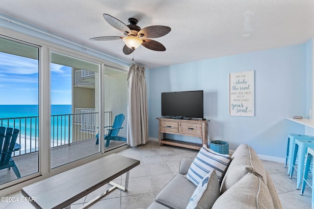 living room featuring ceiling fan, a water view, a textured ceiling, and light tile floors