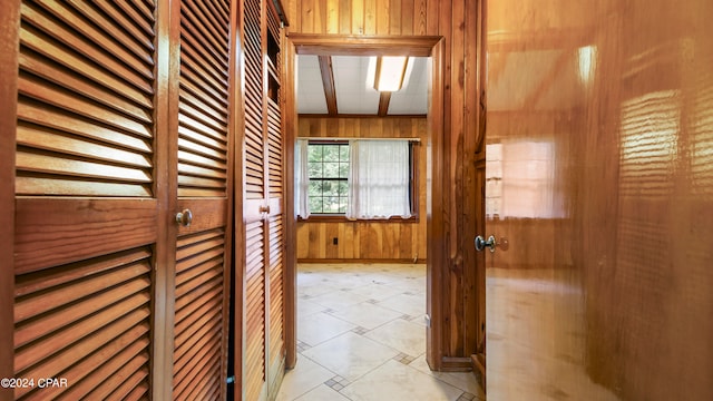 corridor with wooden walls, beamed ceiling, and light tile patterned floors