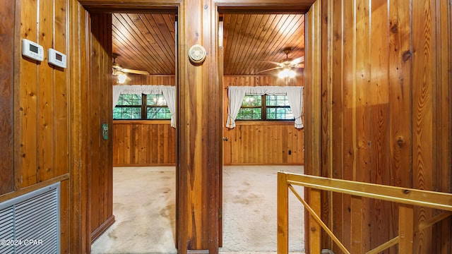 hallway featuring light carpet, wood walls, vaulted ceiling, and wooden ceiling