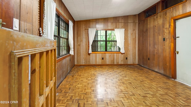 unfurnished room featuring vaulted ceiling, wooden walls, and light parquet floors