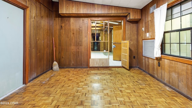 unfurnished room with light parquet floors, wood walls, and lofted ceiling