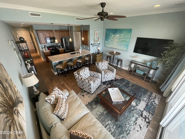 living room with ceiling fan, visible vents, baseboards, dark wood-style floors, and crown molding