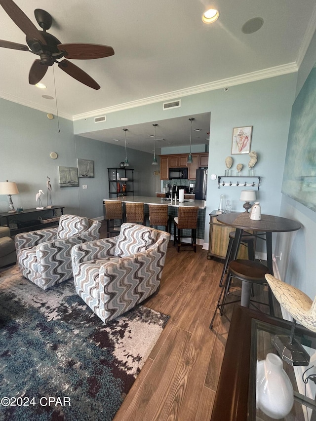 living area featuring dark wood-type flooring, visible vents, ornamental molding, and ceiling fan