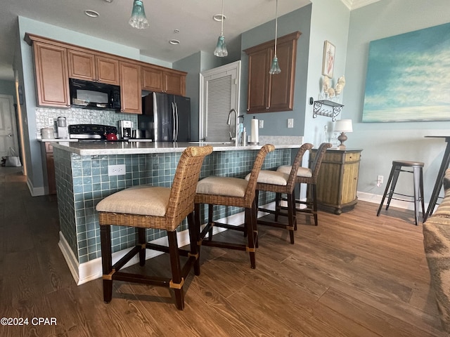 kitchen featuring hanging light fixtures, brown cabinetry, freestanding refrigerator, black microwave, and a peninsula