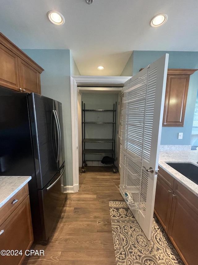 kitchen featuring brown cabinetry, dark wood-type flooring, freestanding refrigerator, a sink, and recessed lighting