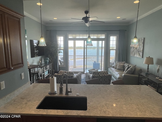 kitchen featuring light countertops, hanging light fixtures, ornamental molding, open floor plan, and a sink