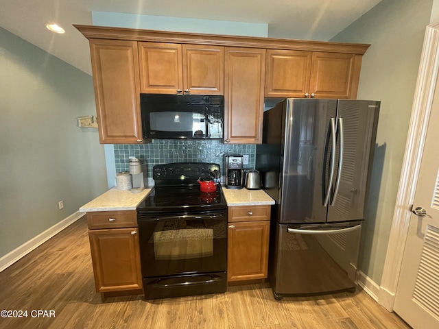 kitchen with light wood-style flooring, brown cabinets, backsplash, and black appliances