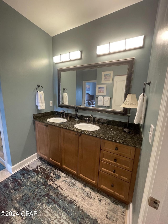 full bath with double vanity, ensuite bath, a sink, and baseboards