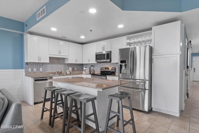 kitchen with a kitchen island, white cabinets, a breakfast bar area, stainless steel appliances, and light stone countertops