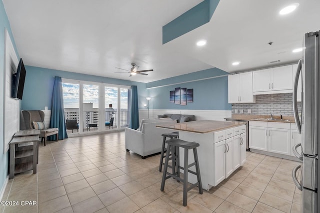 kitchen featuring a kitchen island, ceiling fan, a breakfast bar area, white cabinetry, and stainless steel refrigerator