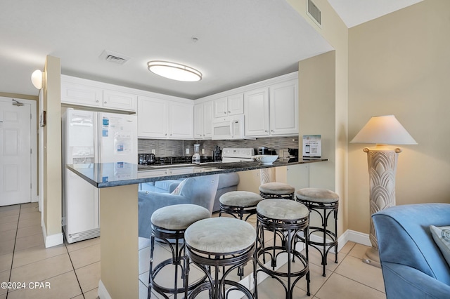 kitchen featuring light tile patterned floors, a kitchen breakfast bar, white cabinets, white appliances, and backsplash