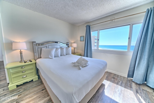 bedroom featuring a water view, a textured ceiling, and hardwood / wood-style flooring