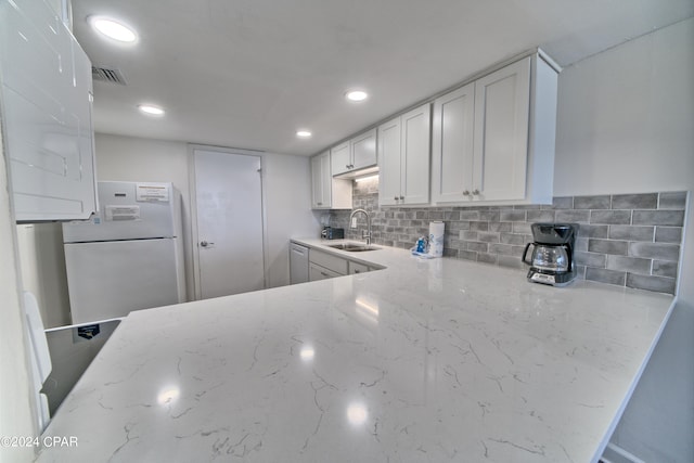 kitchen featuring decorative backsplash, light stone counters, white cabinets, white refrigerator, and sink