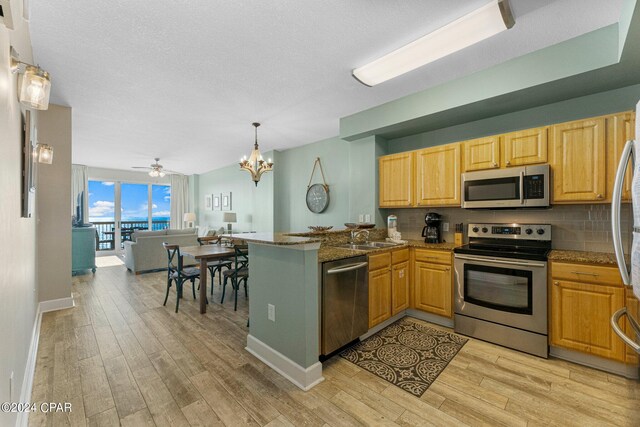 kitchen with dark stone countertops, ceiling fan with notable chandelier, appliances with stainless steel finishes, light hardwood / wood-style flooring, and kitchen peninsula