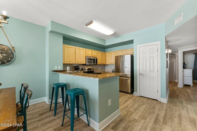 kitchen featuring light hardwood / wood-style flooring, stainless steel appliances, a breakfast bar area, kitchen peninsula, and light stone counters