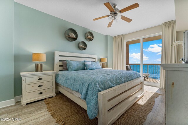 bedroom with access to outside, light hardwood / wood-style floors, ceiling fan, and a water view