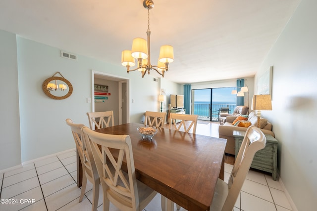 dining space with light tile floors, a notable chandelier, and a water view