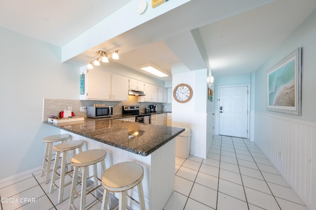 kitchen featuring appliances with stainless steel finishes, kitchen peninsula, light tile flooring, and dark stone countertops