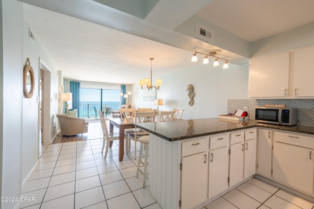 kitchen with backsplash, decorative light fixtures, white cabinets, and light tile flooring