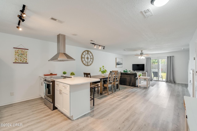 kitchen featuring track lighting, light hardwood / wood-style flooring, electric range, wall chimney exhaust hood, and white cabinetry