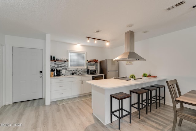 kitchen featuring island exhaust hood, appliances with stainless steel finishes, a kitchen bar, light hardwood / wood-style flooring, and white cabinets