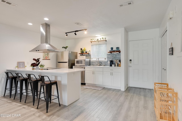 kitchen featuring ventilation hood, sink, appliances with stainless steel finishes, white cabinetry, and a breakfast bar area