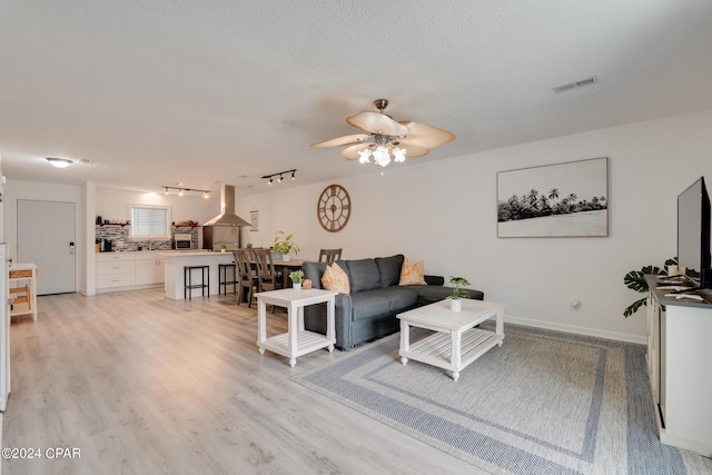 living room featuring rail lighting, ceiling fan, light hardwood / wood-style floors, and a textured ceiling