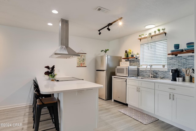 kitchen with exhaust hood, sink, dishwashing machine, a kitchen bar, and white cabinetry