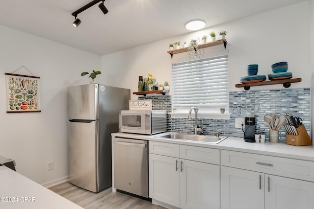 kitchen with backsplash, stainless steel appliances, sink, white cabinets, and light hardwood / wood-style floors