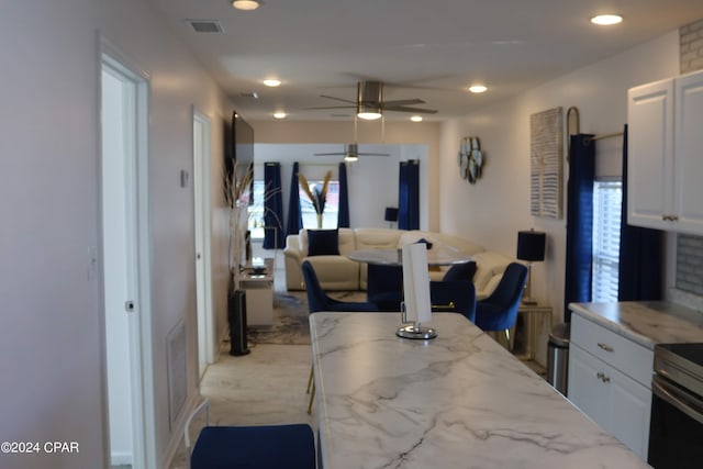 kitchen with light carpet, white cabinets, range, light stone countertops, and ceiling fan