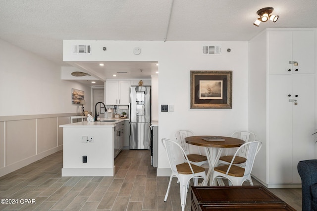 kitchen featuring white cabinetry, stainless steel fridge, sink, light hardwood / wood-style flooring, and a textured ceiling