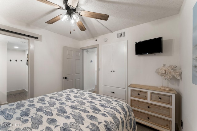 bedroom featuring a barn door, a textured ceiling, and ceiling fan