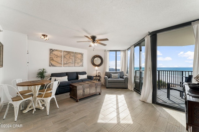 living room with expansive windows, a textured ceiling, ceiling fan, and a water view