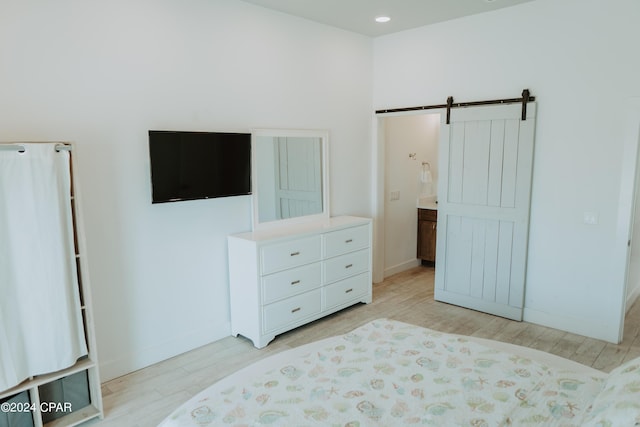 bedroom featuring a barn door, light wood-type flooring, and baseboards