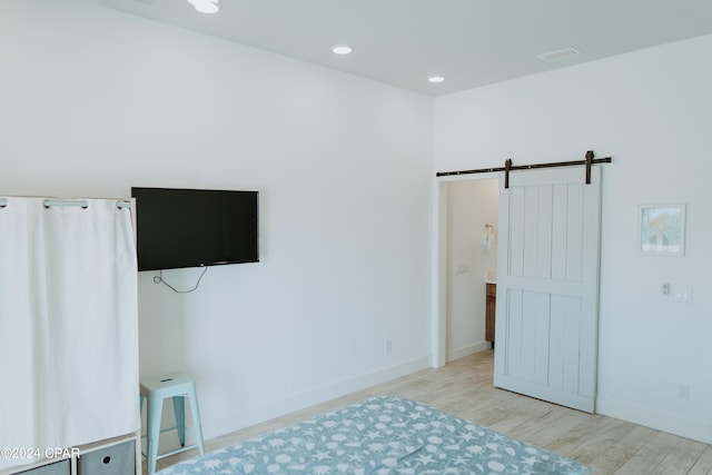 unfurnished bedroom with a barn door, visible vents, baseboards, light wood-style floors, and recessed lighting