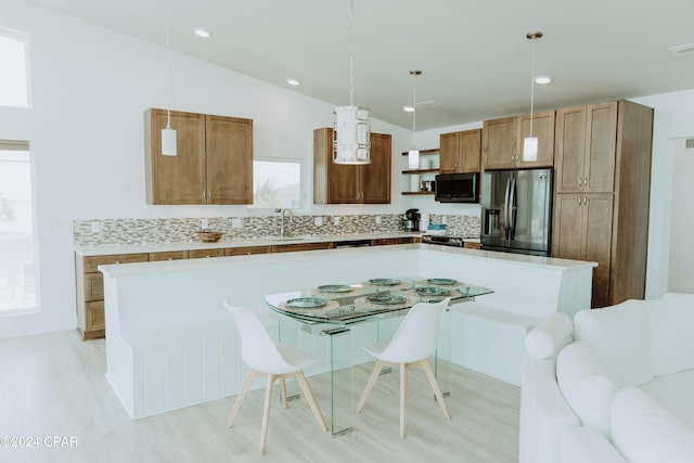 kitchen with a center island, decorative light fixtures, light countertops, brown cabinetry, and stainless steel fridge