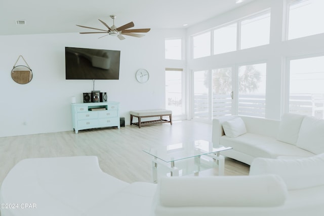 living room featuring a ceiling fan, light wood-type flooring, visible vents, and a towering ceiling